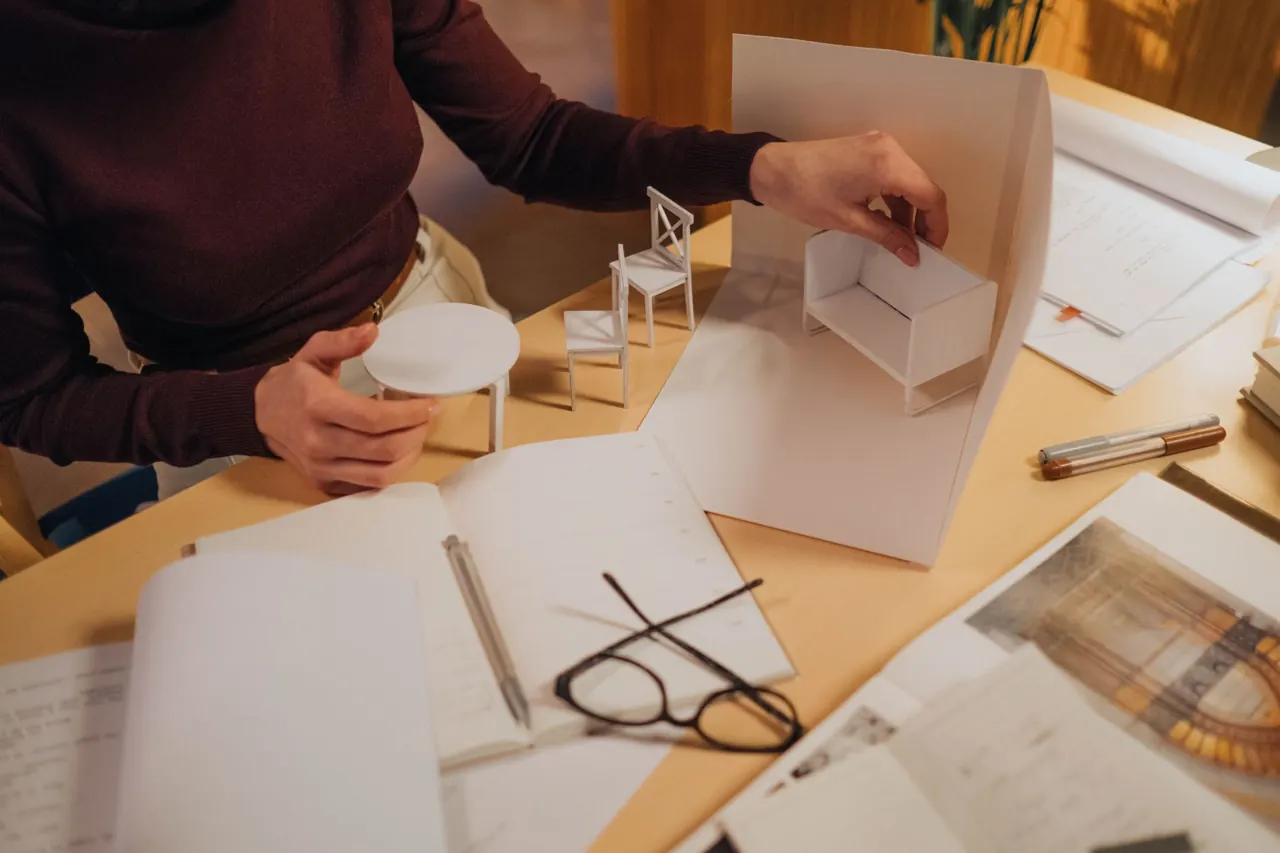 Manos montando una maqueta de cartón sobre planos